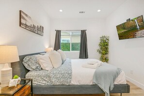 Une chambre à coucher moderne avec un lit, une table de chevet, une lampe et une fenêtre avec des rideaux.
