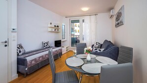 Ein kompakter Wohnraum mit Sofa, Esstisch mit Stühlen, Fernseher und einer kleinen Küchenzeile.