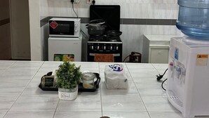 A modern kitchen with white cabinets, a stove, a microwave, and a water dispenser. - Westlands Villas (Nairobi)