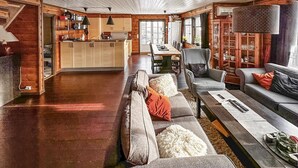 A spacious living room with a large sofa, a dining area with a wooden table, and a kitchen with wooden cabinets and pendant lights. - 4 bedroom awesome home in Rysstad (Rysstad)