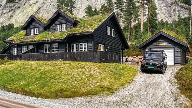 A black cabin with a gravel driveway, a garage, and a parked truck. - 4 bedroom awesome home in Rysstad (Rysstad)