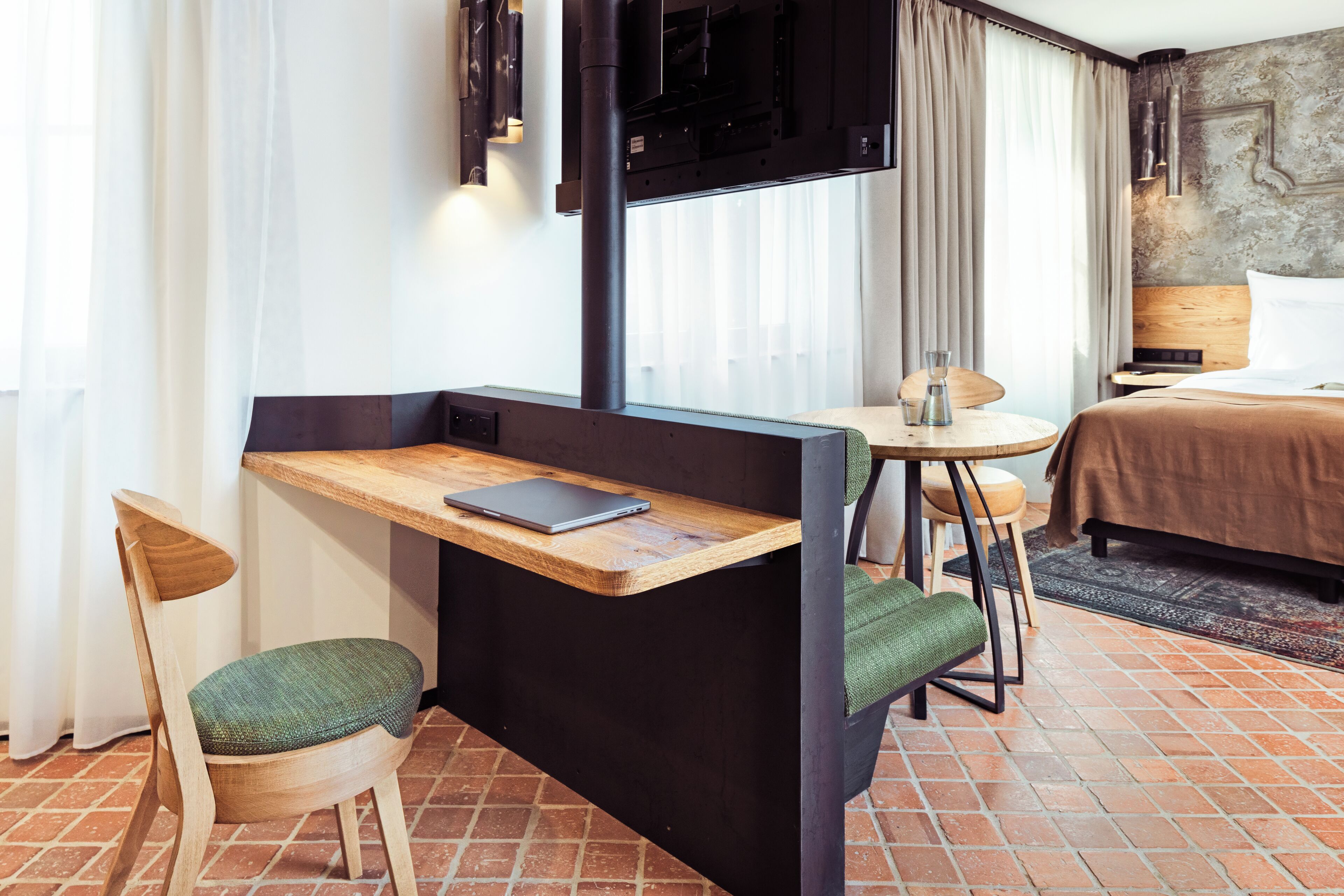 A compact hotel room with a small desk, a chair, a bed, and a TV mounted on the wall.