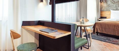 A compact hotel room with a small desk, a chair, a bed, and a TV mounted on the wall.