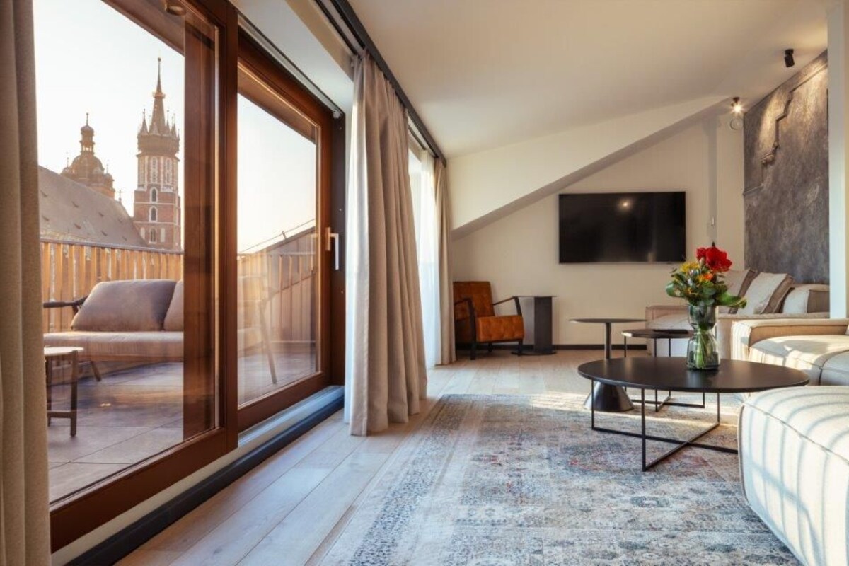 A modern hotel room with a large balcony, a sofa, a coffee table, and a TV mounted on the wall.