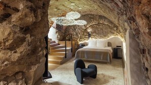 A bedroom with a stone cave-like ceiling, a bed, a chair, and a staircase leading to an upper level. - Nomadic Urban Premium Suites (Kraków)