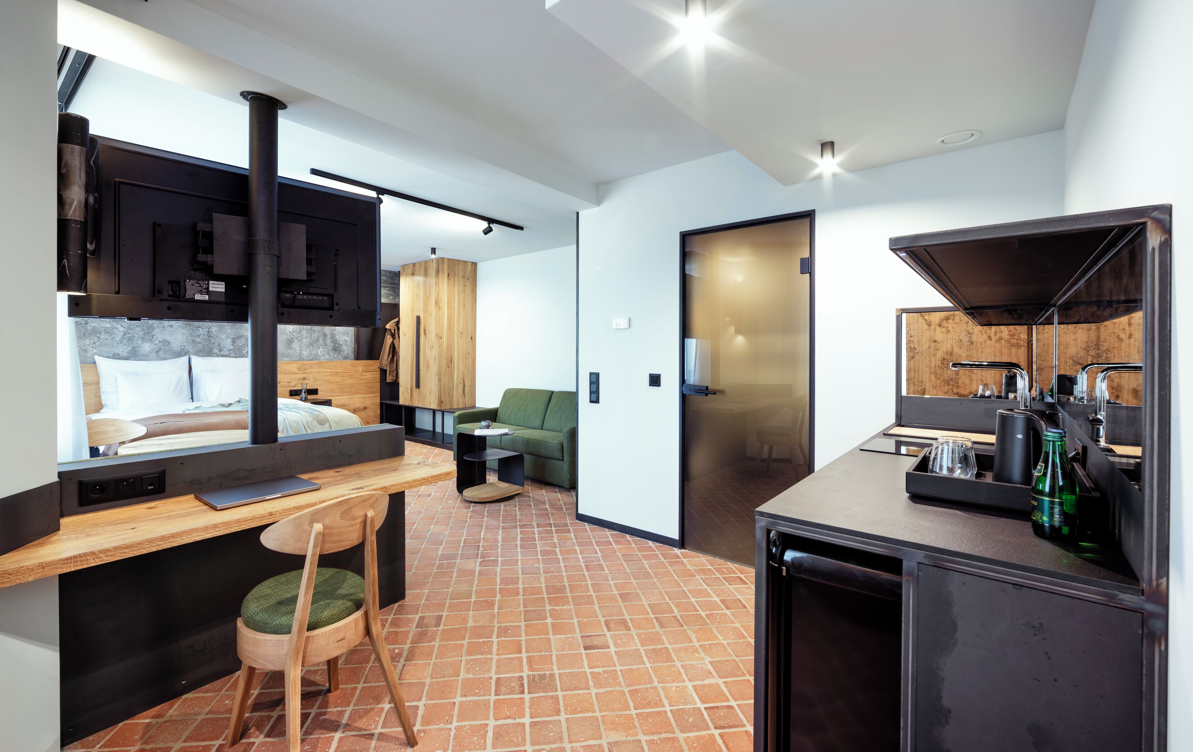 A compact hotel room with a bed, a small seating area, a kitchenette, and a bathroom.