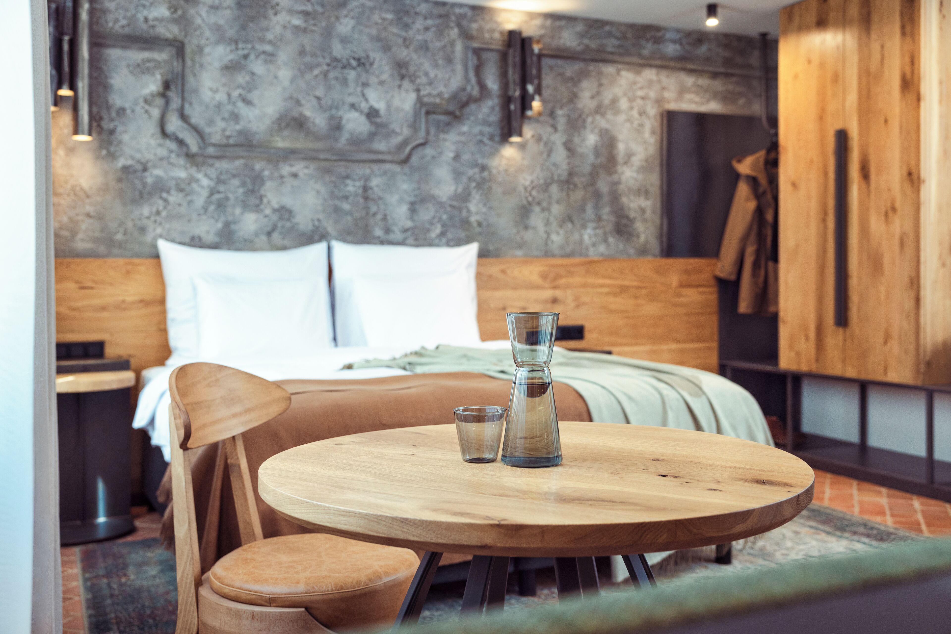 Un dormitorio moderno con una cama de madera, una mesa redonda de madera con dos vasos, y vista al interior de la habitación.