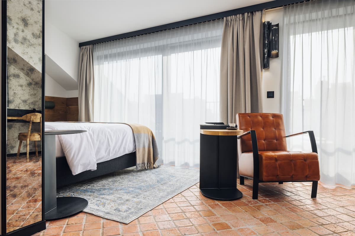 Ein modernes Schlafzimmer mit Bett, Sessel, kleinem Tisch und großem Fenster mit durchsichtigen Vorhängen.