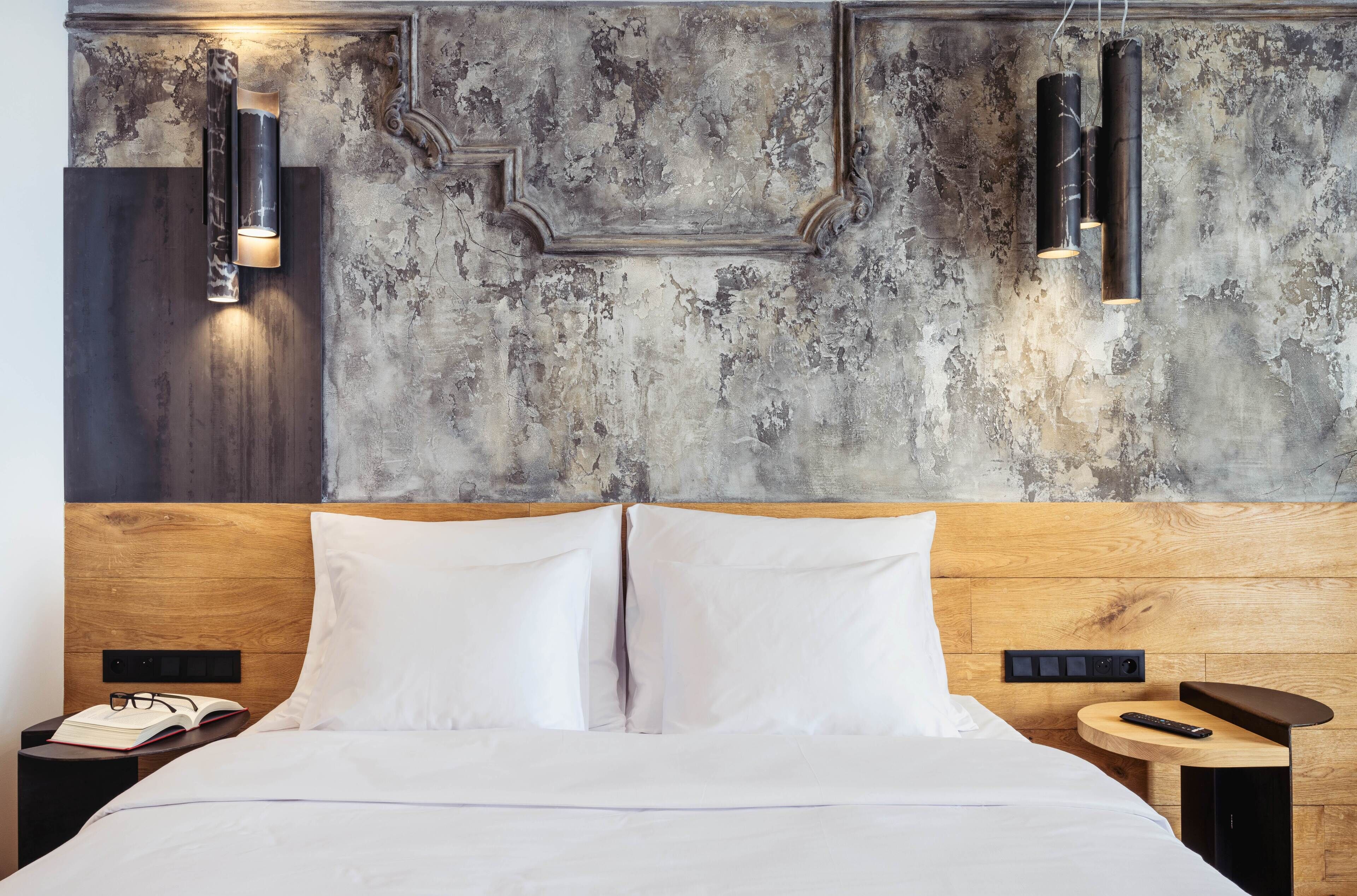 Una habitación de hotel moderna con cabecera de madera, ropa de cama blanca y pared rústica con textura.