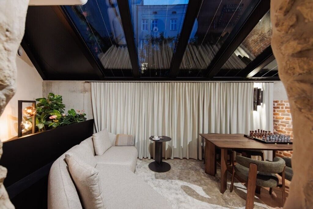 A modern room with a sofa, a small round table, a dining table with chairs, and a view through a skylight.