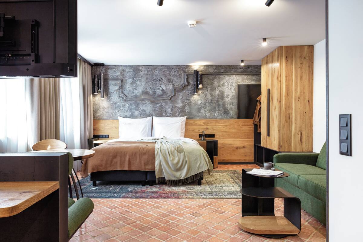 Ein modernes Hotelzimmer mit Bett, einem Holzschrank, einem grünen Sofa, einem kleinen Tisch und einem Schreibtisch.