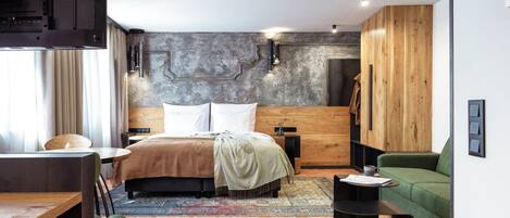 Una habitación de hotel moderna con cama, armario de madera, sofá verde, mesita y escritorio.