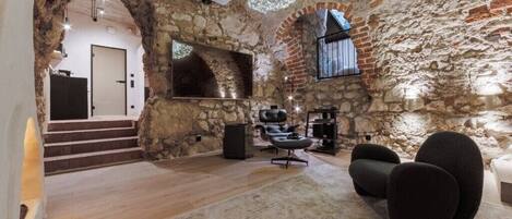 A rustic interior with stone walls, a wooden staircase, a modern sofa, and a projector.