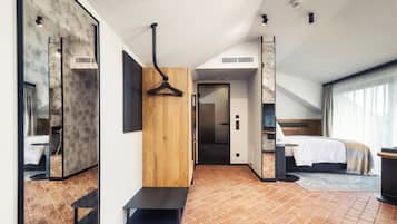 A modern hotel room with a large mirror, a wooden accent wall, a bed with a white duvet, and a small seating area.
