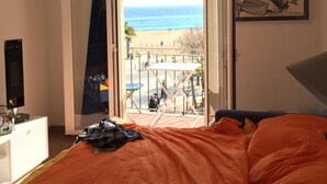 Ein Schlafzimmer mit offener Tür, das auf einen Balkon mit Blick auf Strand und Meer führt.