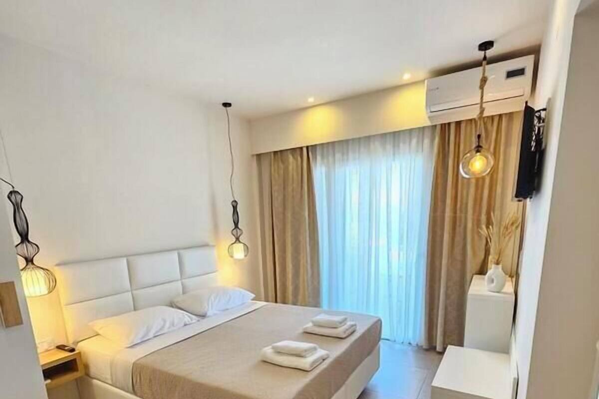 A modern hotel room with a large bed, bedside tables, a desk, and a window with curtains.