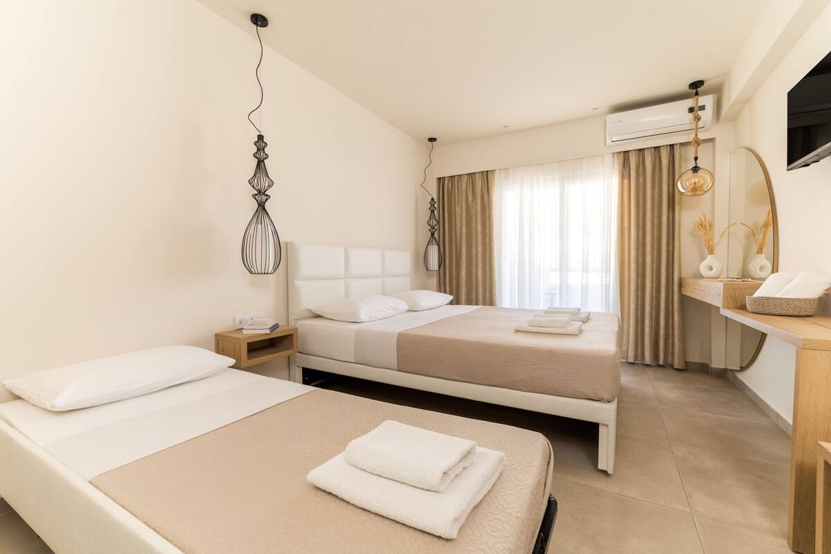 A hotel room with two beds, a desk, a chair, a TV, and a window with curtains.