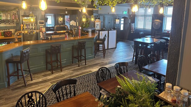 A bar area with a counter, stools, and hanging plants. There are tables and chairs in the dining area. - Sheridans (Wallasey)