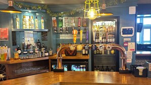 A bar area with a wooden counter, multiple taps, and a variety of bottles. - Sheridans (Wallasey)