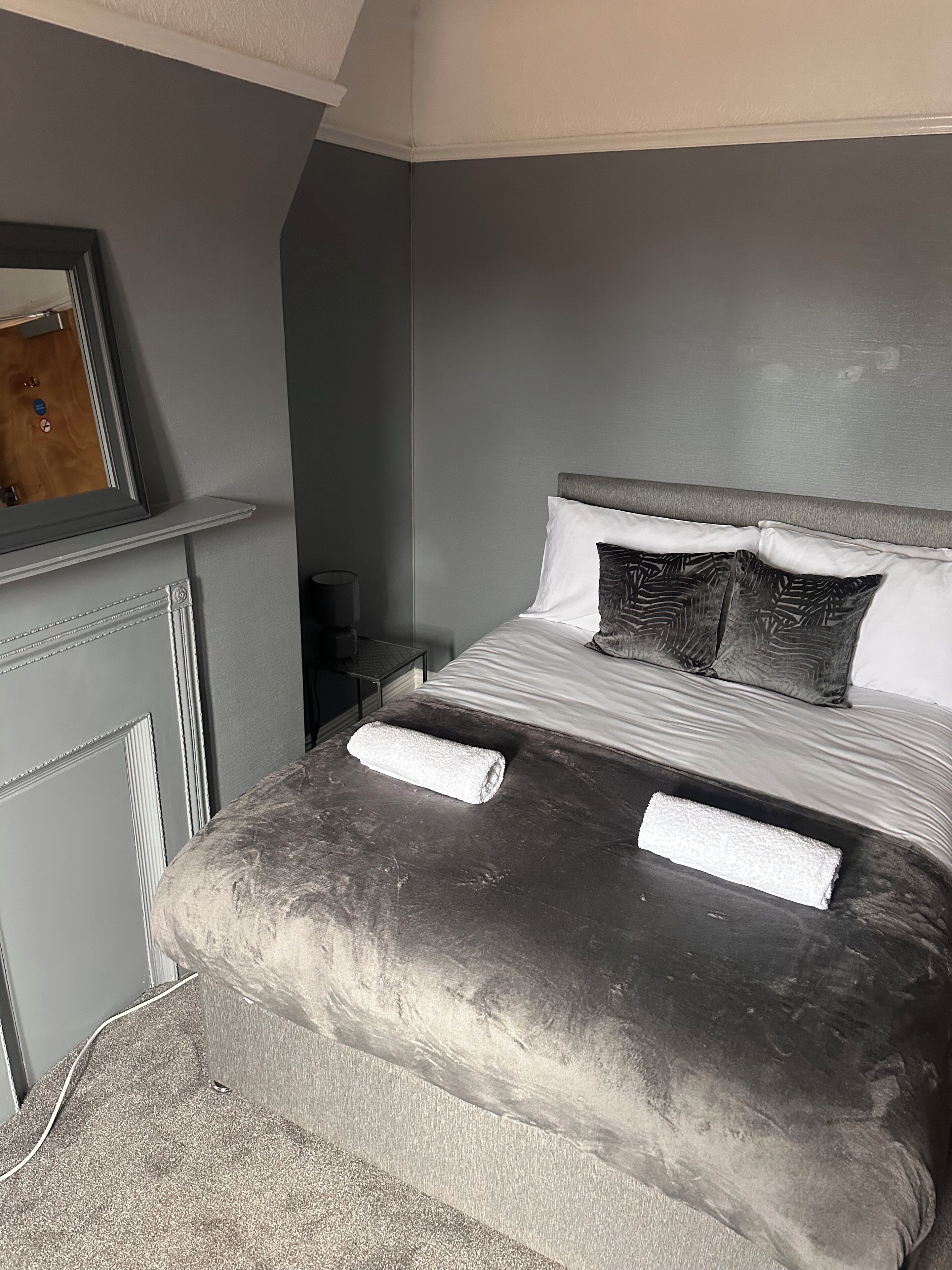 A bedroom with a bed, pillows, a nightstand, and a mirror.