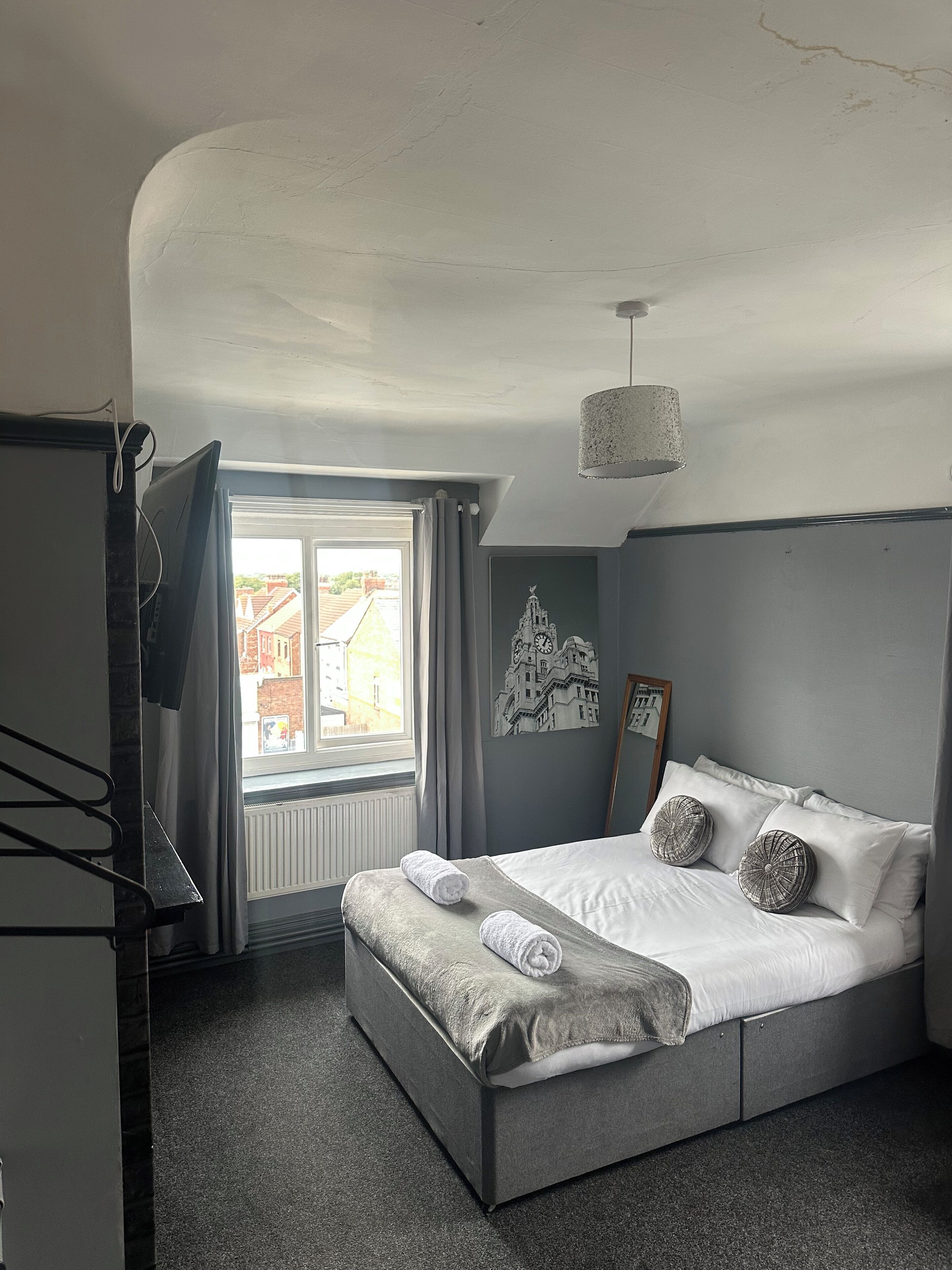 Quarto com cama, janela, radiador e um quadro fixado na parede.