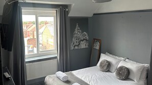 A modern bedroom with a large bed, grey walls, a window with curtains, a radiator, and a wall clock. - Sheridans (Wallasey)