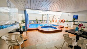 Un espace piscine comprenant un jacuzzi circulaire, des chaises longues et un panneau indiquant les règles d’utilisation de la piscine.