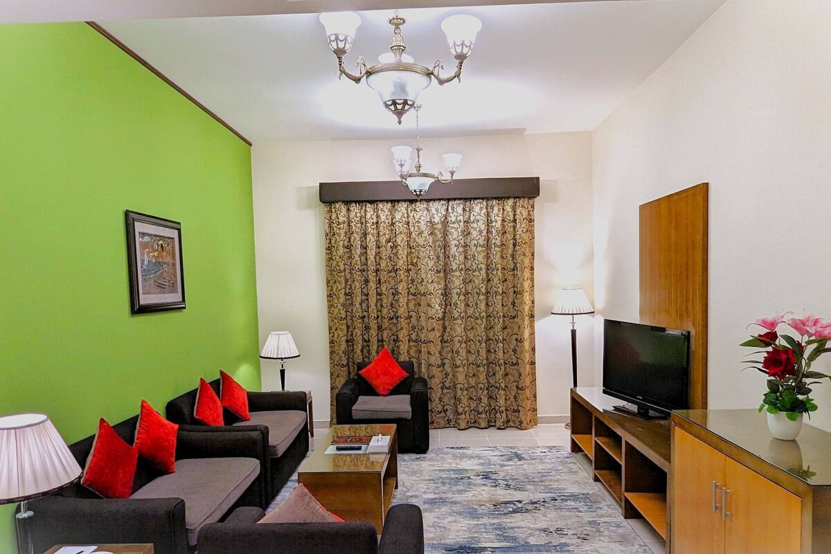 A living room with a green wall, a sofa set, a television, and a cabinet.