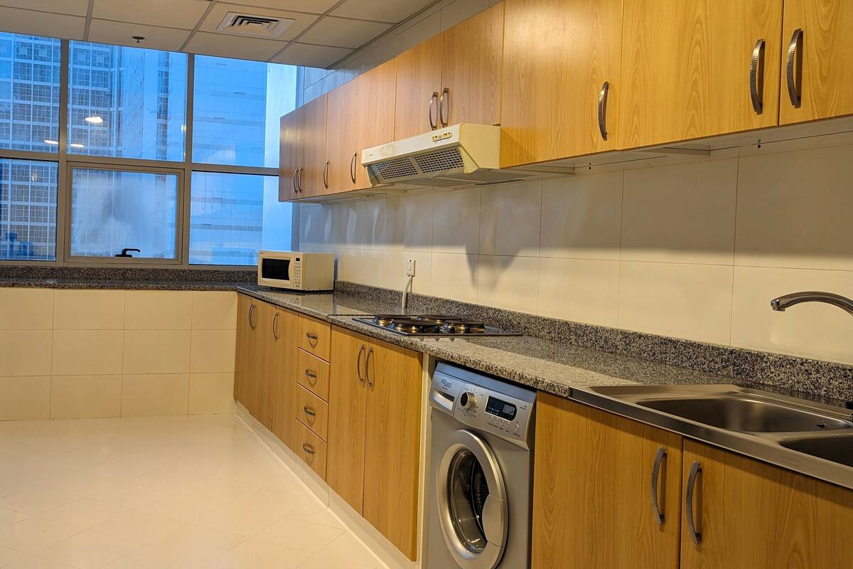 A modern kitchen with wooden cabinets, a built-in microwave, a stainless steel sink, and a front-loading washing machine.