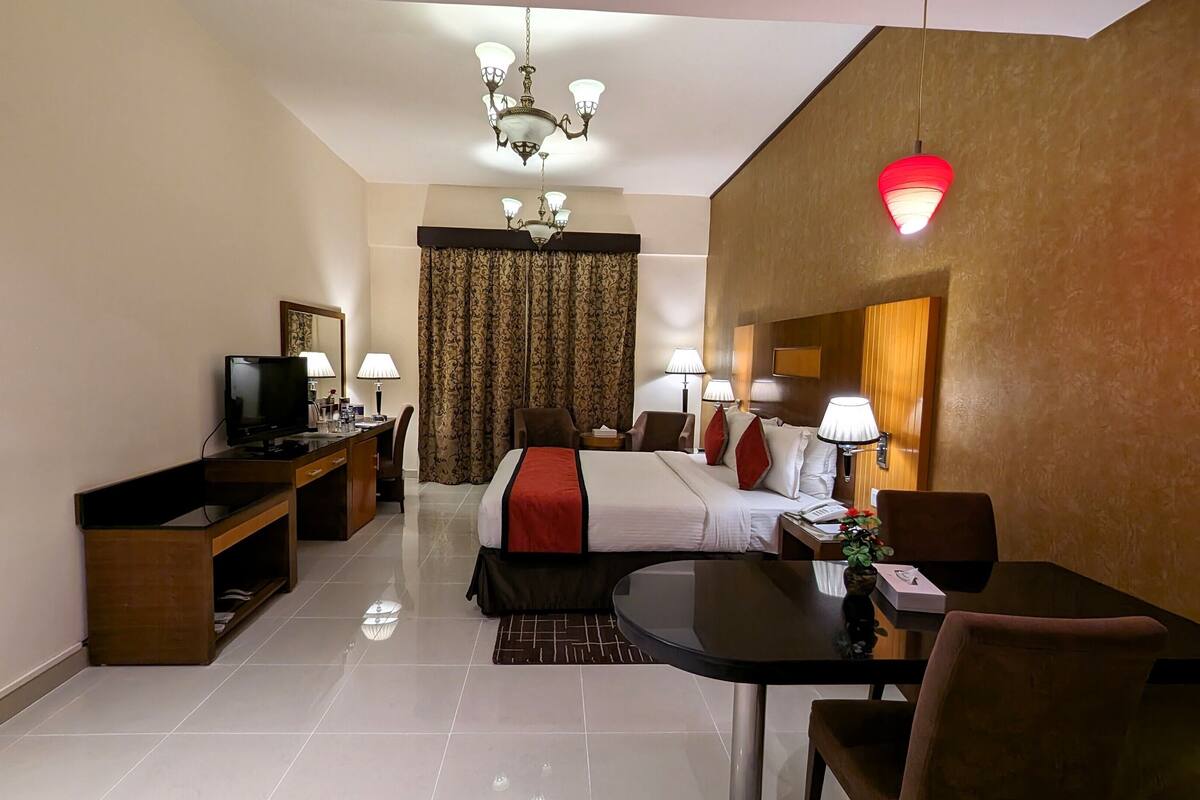 A hotel room with a bed, desk, television, lamps, and a chandelier.