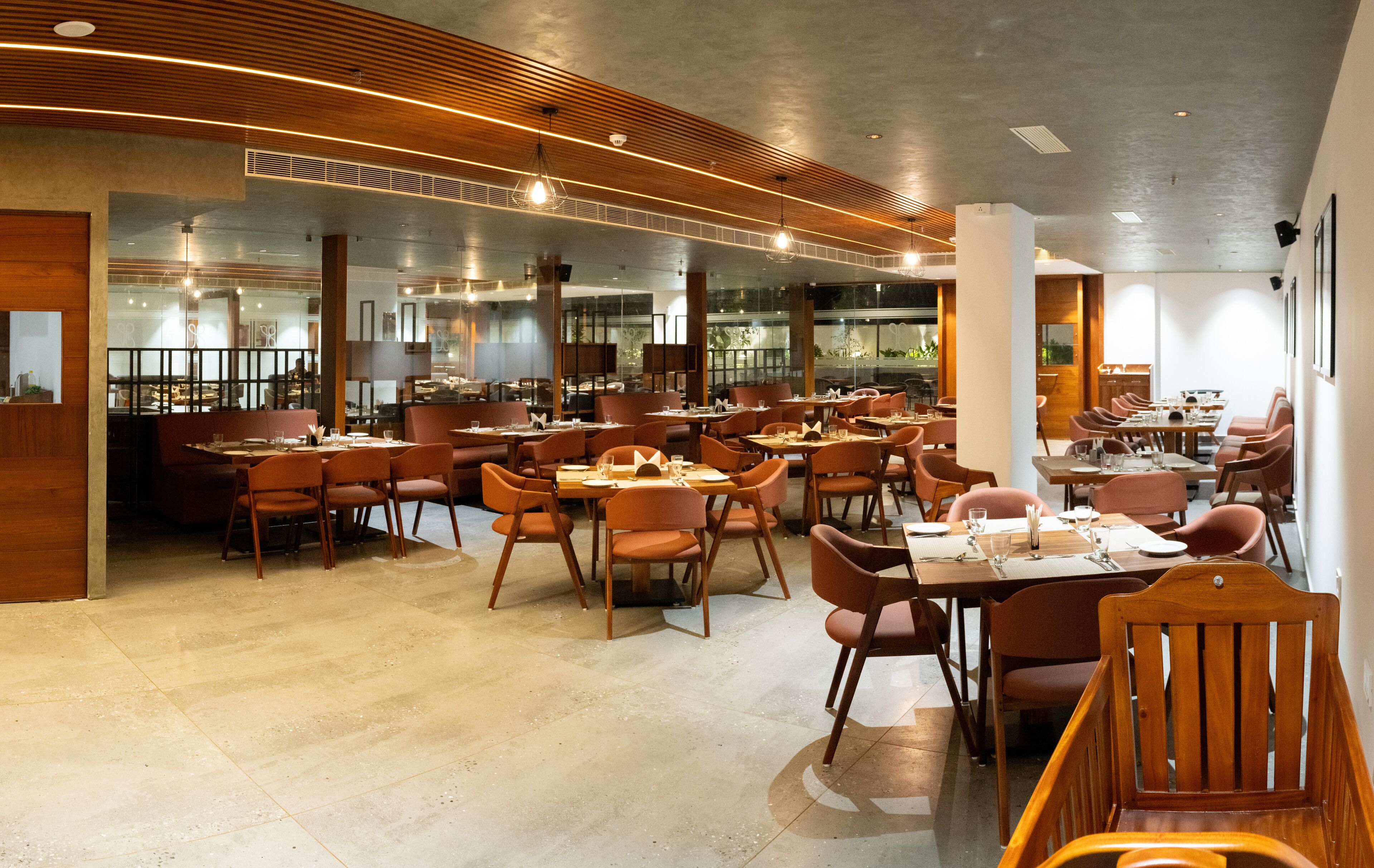 A spacious restaurant with multiple dining areas, large windows, and modern wooden accents.