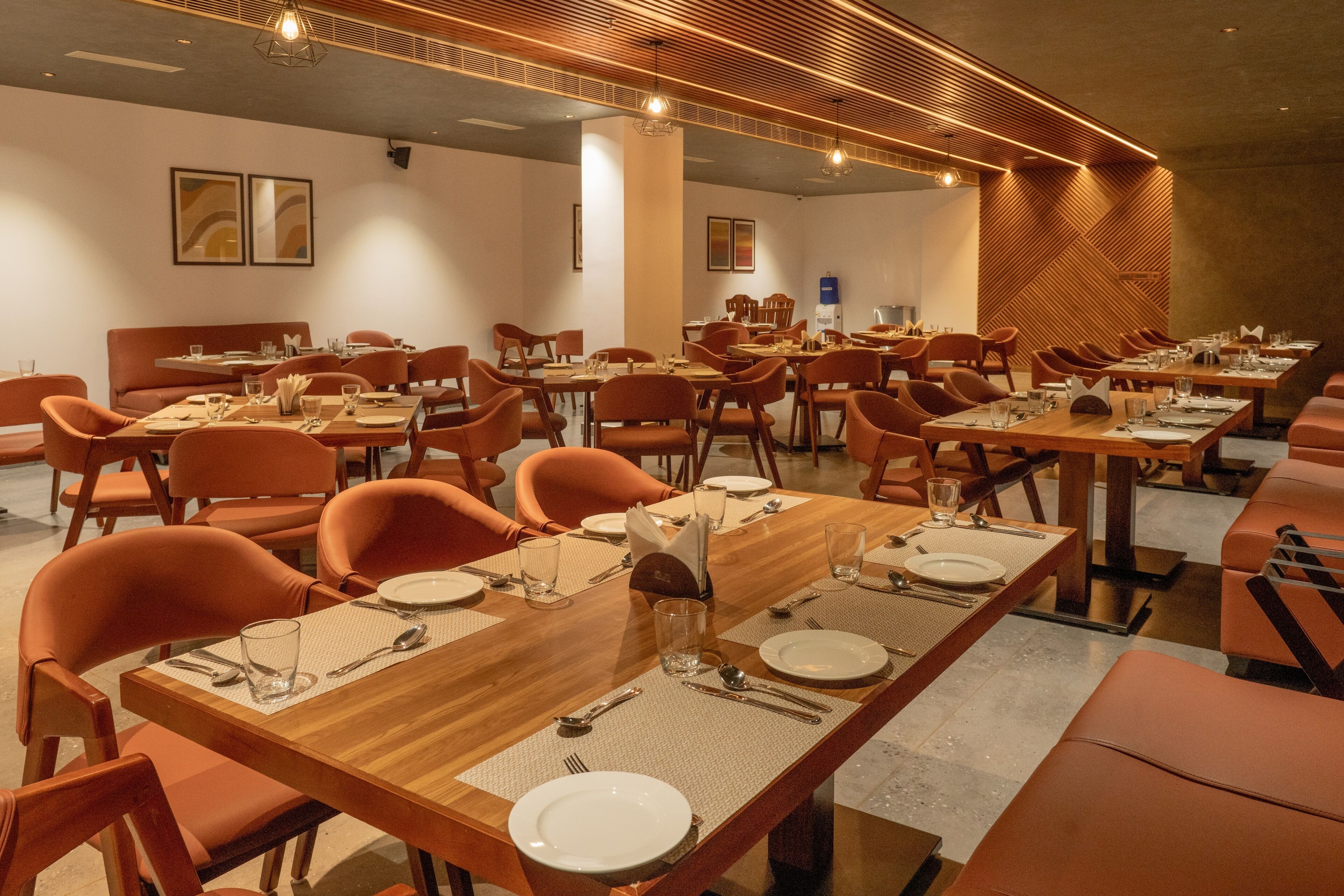 Un comedor amplio con varias mesas y sillas, que presenta un diseño moderno con detalles de madera e iluminación cálida.