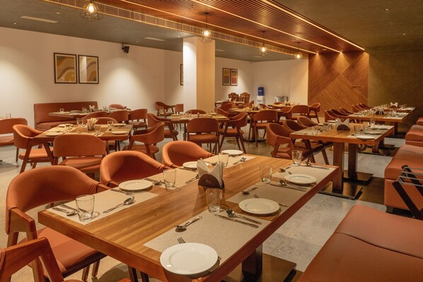 A spacious dining area with multiple tables and chairs, featuring a modern design with wooden elements and warm lighting.