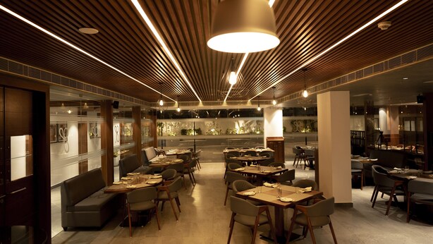 Un restaurant moderne avec des plafonds lambrés en bois, des luminaires suspendus et un espace de restauration central agrémenté de tables et de chaises.