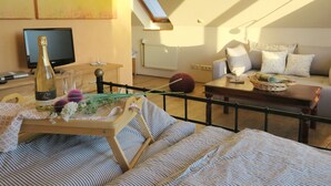 A cozy living room with a bed, a television, a bottle of wine, and a window with a view of trees. - Unsere Casita- Idylle in Ruhe und mit Kleinem Beach (Apensen)