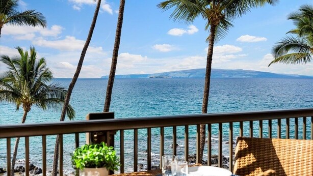 Un balcón con vistas al océano, palmeras y un comedor.