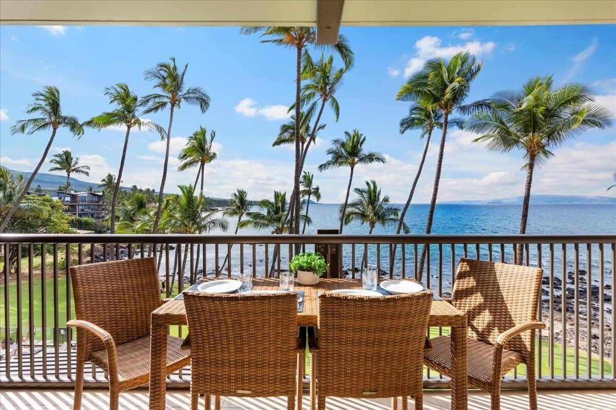 A balcony with wicker furniture and a view of the ocean and palm trees.
