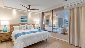 Una habitación de hotel con una cama grande, ventilador de techo, balcón con vistas y aire acondicionado.