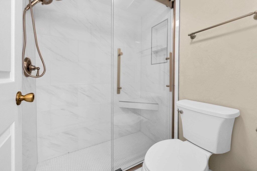 A bathroom with a glass shower enclosure, a white toilet, and a beige wall.