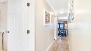 A hallway with a white door, beige walls, and a dining area with a table and chairs. - South Seas Bayside Villa 5226 1 Bedroom Condo by RedAwning (Captiva)