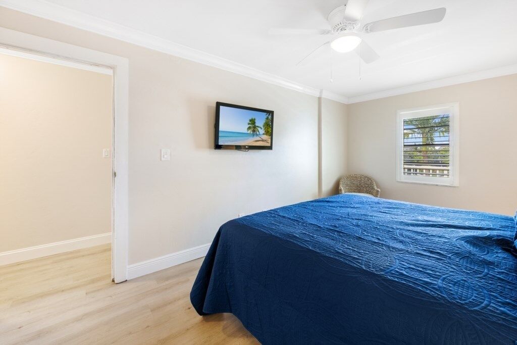 Una camera da letto con un letto, una ventola a soffitto, una televisione a parete e una finestra con persiane.