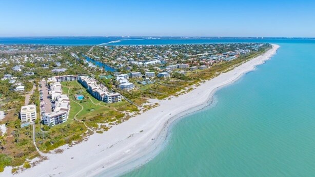 An aerial view of a coastal resort with beachfront properties, a marina, and a clear blue sky. - Loggerhead 424 2 Bedroom Condo by RedAwning (Sanibel)
