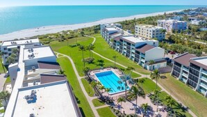 A resort with a swimming pool surrounded by palm trees, a beach, and multiple hotel buildings. - Loggerhead 424 2 Bedroom Condo by RedAwning (Sanibel)