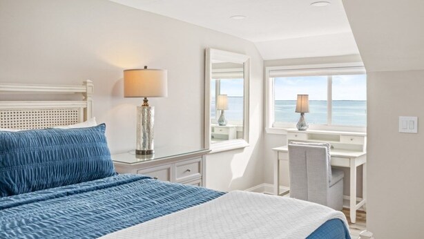 Ein Schlafzimmer mit Bett, Schreibtisch, Stuhl, Lampe und Meerblick.