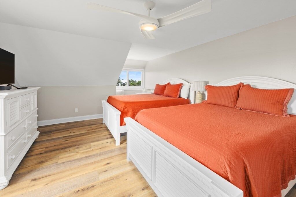 A bedroom with two beds, a ceiling fan, and a dresser.