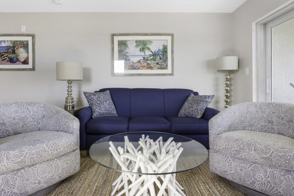 Een woonkamer met een blauwe bank, gestreept fauteuils, een glazen salontafel en twee ingelijste foto's aan de muur.