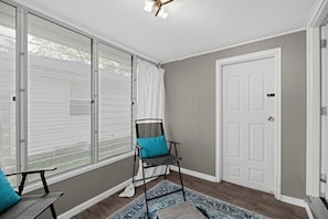 A room with a sliding glass door, a white door, a chair with a cushion, a patterned rug, and a ceiling light fixture. - Damaged Shower (Kalamazoo)