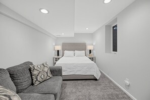 A bedroom with a bed, two bedside tables with lamps, a grey sofa with patterned cushions, and a carpeted floor. - Damaged Shower (Kalamazoo)