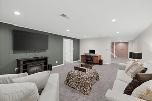 A modern living room with a flat-screen TV, a fireplace, a desk with a chair, and a staircase leading to another level. - Damaged Shower (Kalamazoo)