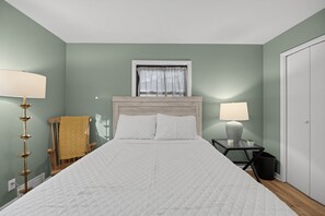 A neatly arranged bedroom with a large bed, two bedside lamps, a window with curtains, and a bedside table with a lamp and a small plant. - Damaged Shower (Kalamazoo)